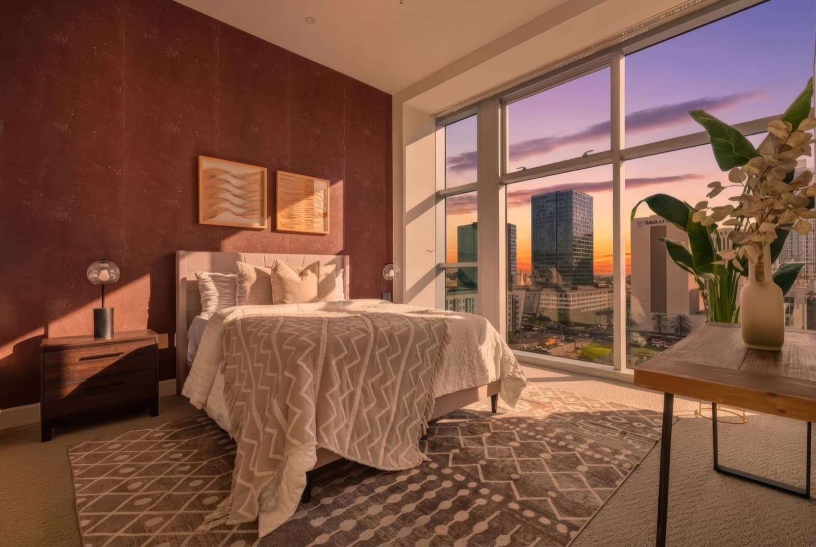 The same primary bedroom at dusk, with the city lights starting to show through the window